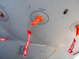 Protective orange plugs with red remove before flight tags installed under aircraft fuselage for maintenance safety