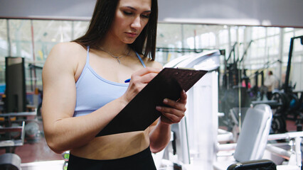 Fitness trainer documenting workout plan in modern gym during afternoon session