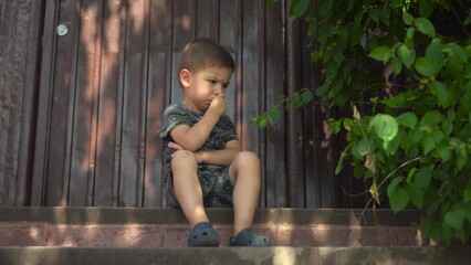 Child is angry and crosses arms showing frustration on a porch during a hot summer day in dark clothes