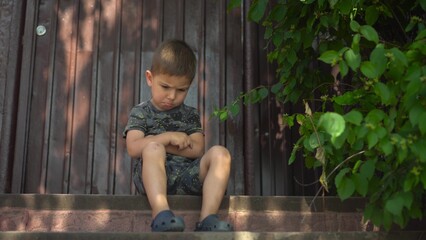 Child is angry and crosses arms showing frustration on a porch during a hot summer day in dark clothes