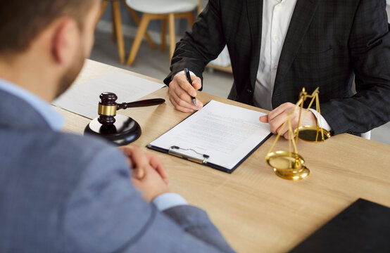Fototapeta Male lawyer discussing contract with man client going to sign documents in office. Attorney having a meeting sitting at desk with a judge's gavel and scales. Legal law and advice concept.