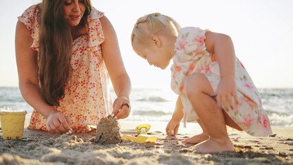 Mother and daughter enjoy building a sandcastle together on a sunny beach in the late afternoon...