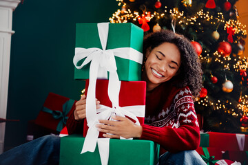 Joyful woman hugs festive gifts beside a glowing Christmas tree creating a warm merry home scene