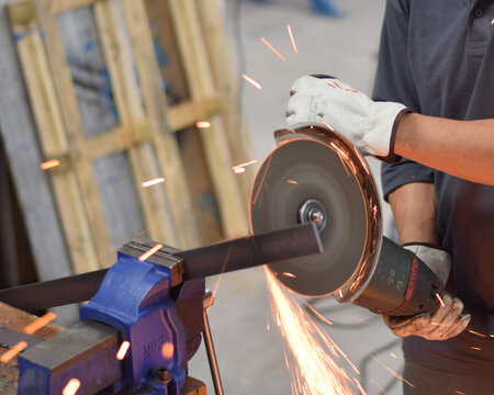 Worker cutting metal with angle grinder and flying sparks - Powered by Adobe