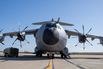 Close frontal perspective of a turboprop military transport aircraft with four propeller engines parked on an airfield