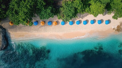 Aerial view of a sandy beach with a row of alternating blue and orange umbrellas surrounded by lush green trees and clear turquoise ocean water