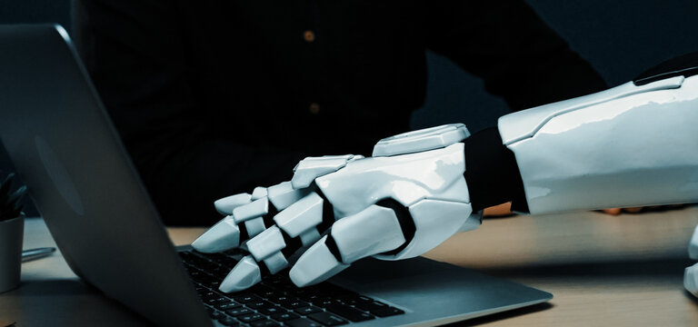 A close-up of a robotic hand interacting with a laptop, showcasing the blend of advanced technology and human-like capabilities in a modern office environment.Noogenesis