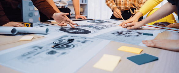 A diverse team engages in collaborative brainstorming while reviewing detailed blueprints and graphics on a table, highlighting innovation and teamwork in a modern office environment. SACTR