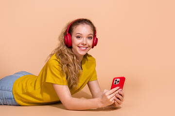 Smiling young woman wearing headphones and using a smartphone on a beige background