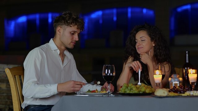 Close up of happy couple in love sitting outside at night romantic date eating delicious food. Handsome husband feeding beautiful young wife on date dinner. Happy marriage - Powered by Adobe