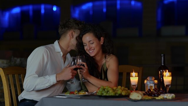 Close up of happy passionate couple in love drinking wine at romantic date and flirting. Handsome loving husband whispering on ear beautiful young wife. Dating concept