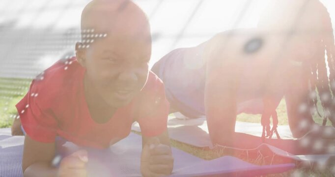 Father guiding son holding forearm plank on grass, encouraging while map or code overlaying faces
