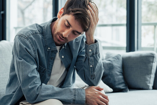Tired Caucasian young man sit on couch touch massage head suffer from headache or migraine, exhausted millennial male feel fatigue having sleep deprivation or dizziness, eyesight problem concept
