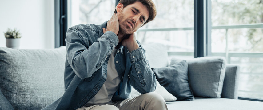 Upset tired young man feeling pain massaging stiff neck rubbing tensed muscles to relieve back ache joint shoulder discomfort after long sedentary work in incorrect posture, fibromyalgia concept