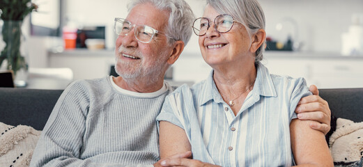 Dreamy middle aged senior loving retired family couple looking in distance, planning common future or recollecting memories, enjoying peaceful moment relaxing together on cozy sofa in living room