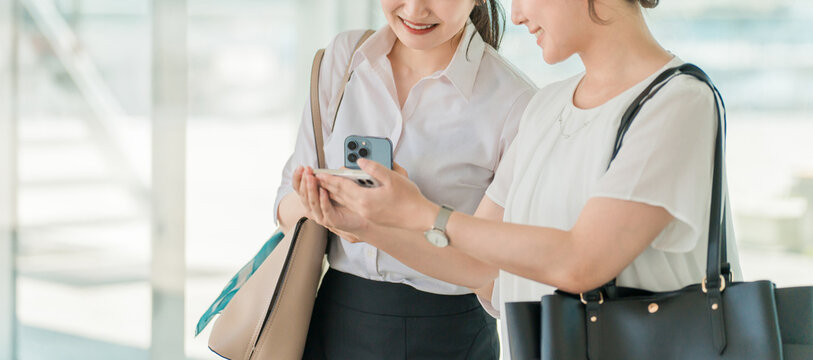 A businesswoman walking with a smile in a business district or office district while looking at her smartphone (commuting, going to work, sales)