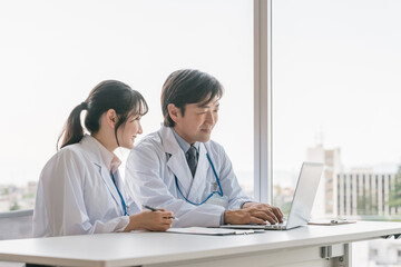 Obraz premium A male supervising doctor and a female trainee doctor are receiving training while looking at electronic medical records on a computer 