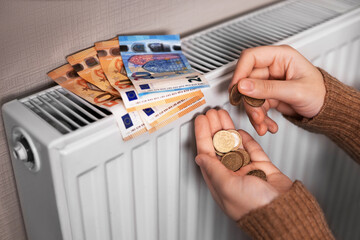 A girl in a sweater is counting money by the radiator The room is cold, so the heating is needed.