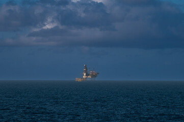 Offshore oil platform, drilling rig, and supply boat at twilight