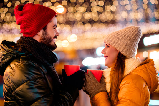 Playful couple share warm drinks under festive city lights during a cozy winter holiday evening
