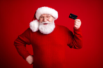 Santa in red sweater holds a card smiles large against festive red background for holiday shopping...