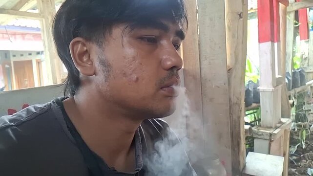 A young man relaxing while smoking a cigarette outdoors, enjoying peaceful time alone with natural light and calm atmosphere.