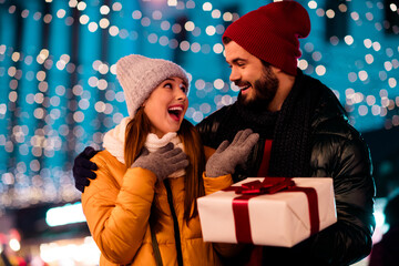 playful couple surprises each other with a gift under sparkling city lights during a merry Xmas...