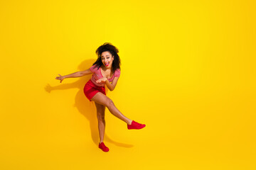 Cheerful woman in red striking a playful pose against yellow background, expressing joy and energy in stylish fashion.