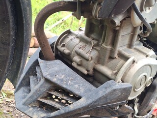 Detailed close-up of a 150cc motorcycle engine and exhaust pipe covered in dust and mud, showing mechanical parts and rugged outdoor texture.