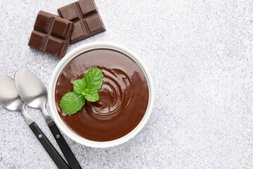 Melted chocolate with mint in bowl, pieces and spoons on light grey table, flat lay. Space for text