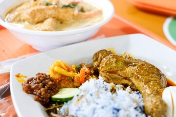 A bowl of laksa and plate of chicken rendang nasi lemak with sambal, peanuts and anchovies, pickles, egg and blue butterfly pea flower coconut rice at Old Nyonya, a hawker stall at Maxwell, Singapore
