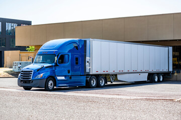 High cab blue big rig semi truck with dry van semi trailer unloading delivered cargo standing in warehouse dock © vit