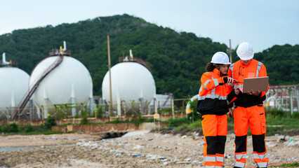 Petrochemical engineers in PPE conduct a site survey near LNG storage spheres. They use a laptop for data analysis and a radio for comms at the coastal refinery terminal.