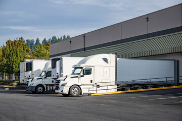 Fototapeta premium Long and local haulers big rig white semi truck with refrigerated semi trailer loading cargo standing in warehouse dock gates