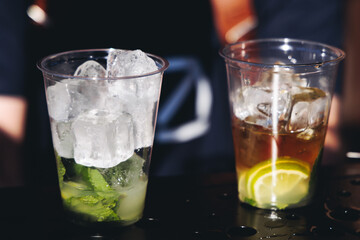 Barman mixing liquor beverages and alcohol drinks in plastic cups, bartender working, beautiful row line of different coloured cocktails on open air summer party in a bar, catering on banquet event