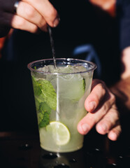 Barman mixing liquor beverages and alcohol drinks in plastic cups, bartender working, beautiful row line of different coloured cocktails on open air summer party in a bar, catering on banquet event