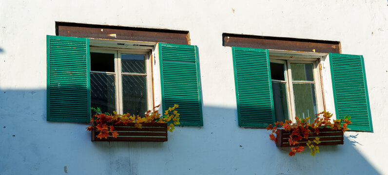 Two windows with green shutters and flower boxes on white wall - Powered by Adobe