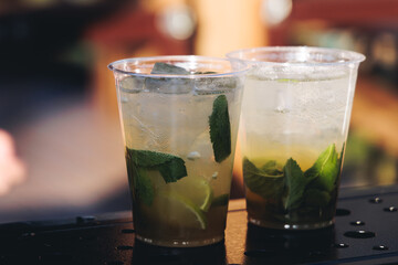Barman mixing liquor beverages and alcohol drinks in plastic cups, bartender working, beautiful row line of different coloured cocktails on open air summer party in a bar, catering on banquet event