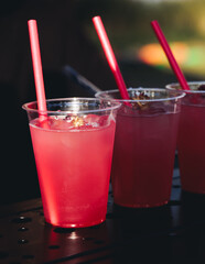 Barman mixing liquor beverages and alcohol drinks in plastic cups, bartender working, beautiful row line of different coloured cocktails on open air summer party in a bar, catering on banquet event