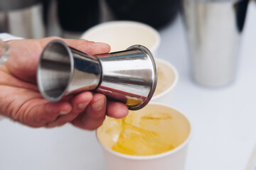 Barman mixing liquor beverages and alcohol drinks in plastic cups, bartender working, beautiful row line of different coloured cocktails on open air summer party in a bar, catering on banquet event