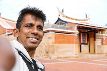 Happy middle aged man taking selfie with Fujian-style house during travel. 