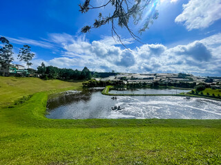 A serene pond with aerators bubbles under a bright sky, bordered by green fields and plastic-covered crops—nature and agriculture in harmony