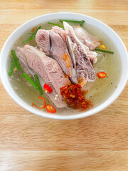 A bowl of hủ tíu xương with tender pork ribs in clear broth, topped with chili paste, green onions, and red chili—spicy, savory, and comforting