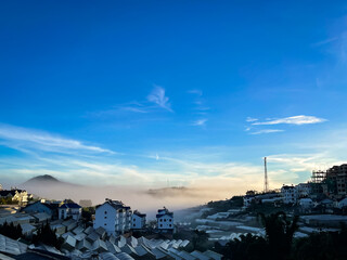 A panoramic view of Da Lat city under clear blue skies with soft fog hugging greenhouses and houses. Peaceful and refreshing morning