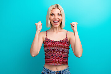 Young woman with a joyful expression wearing a patterned tank top stands against a bright turquoise...