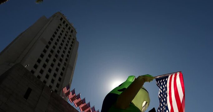 Los Angeles, California, USA - October 18, 2025: A protester dressed in an inflatable frog outfit waves an upside down flag and 8647 sign.