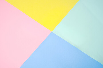 Soft pastel sheets in yellow, pink, mint green, and light blue arranged in a geometric cross pattern, forming a clean and minimal abstract background with gentle color harmony.