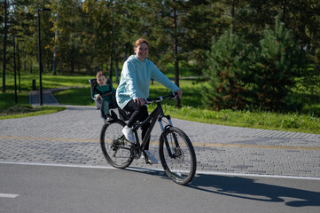 Fototapeta premium Caucasian woman rides bicycle with one-year-old son in park. 