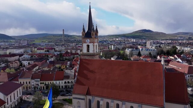 Aerial shot of the Renaissance and Gothic tower of the Bistrita Evangelical Church. The camera moves in smoothly focusing on the clock face, the tall spire, and the surrounding Transylvanian cityscape