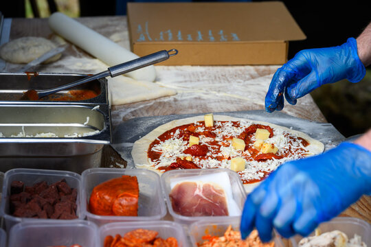 Chef placing fresh toppings on rolled out pizza dough on paddle to make individual wood fired pizza in food truck outdoors
 - Powered by Adobe